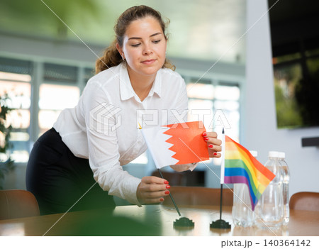 Young woman putting Bahrain and LGBT flags on table in office Young woman putting Bahrain and LGBT flags on table in office 140364142