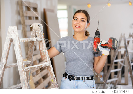 Smiling woman holding drill, repair works in apartment Smiling woman holding drill, repair works in apartment 140364475