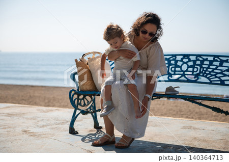 Mother Holding Toddler on Seaside Bench During Summer Vacation Mother Holding Toddler on Seaside Bench During Summer Vacation 140364713