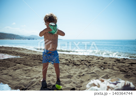Child Pouring Sand From Bucket on Sunny Beach Child Pouring Sand From Bucket on Sunny Beach 140364744
