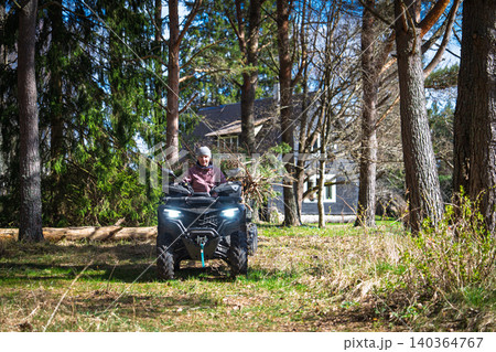 Woman riding an ATV quad bike through a forest, enjoying an outdoor adventure in Estonia 140364767