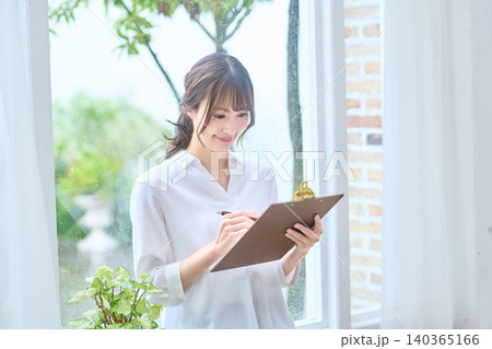 クリップボードに記入しながら微笑む女性 クリップボードに記入しながら微笑む女性 140365166