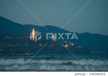illuminated Lady Buddha statue and Linh Ung Pagoda above coastline with sea waves and mountains in Da Nang, Coastal landscape with ocean waves and Son Tra Peninsula at night, Danang Vietnam illuminated Lady Buddha statue and Linh Ung Pagoda above coastline with sea waves and mountains in Da Nang, Coastal landscape with ocean waves and Son Tra Peninsula at night, Danang Vietnam 140366928