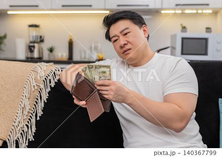 Asian man checks wallet sees only small dollar bills frowns and sets saving goal for budget plan new Asian man checks wallet sees only small dollar bills frowns and sets saving goal for budget plan new 140367799