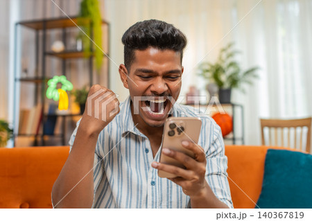 Indian man celebrates online win after mobile alert reads news on smartphone joyful happy reaction Indian man celebrates online win after mobile alert reads news on smartphone joyful happy reaction 140367819