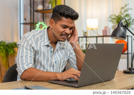 Indian man with laptop suffers headache rubs temples squints at screen needs rest break and relief Indian man with laptop suffers headache rubs temples squints at screen needs rest break and relief 140367820