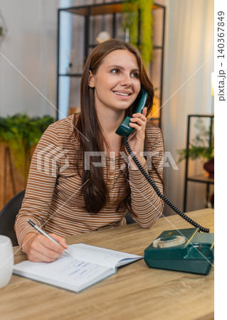 Young woman calls on retro landline phone 90s nods writes address in notebook and says thank you yes Young woman calls on retro landline phone 90s nods writes address in notebook and says thank you yes 140367849