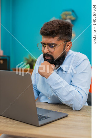 Indian man typing laptop stops rubs chin ponders vital idea focused creative decision moment indoors 140367934