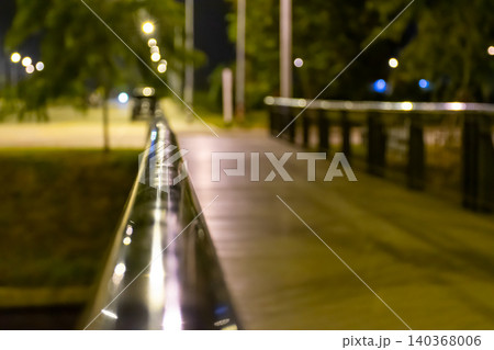 Nighttime walkway illuminated street lights metal railing creating soft bokeh reflections urban perspective peaceful outdoor atmosphere Nighttime walkway illuminated street lights metal railing creating soft bokeh reflections urban perspective peaceful outdoor atmosphere 140368006