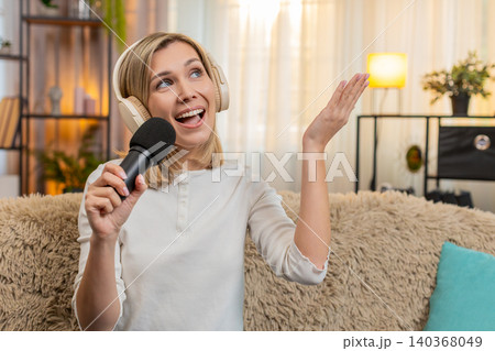 Adult woman singing with headphones and microphone at home dancing joyfully feeling like a superstar Adult woman singing with headphones and microphone at home dancing joyfully feeling like a superstar 140368049