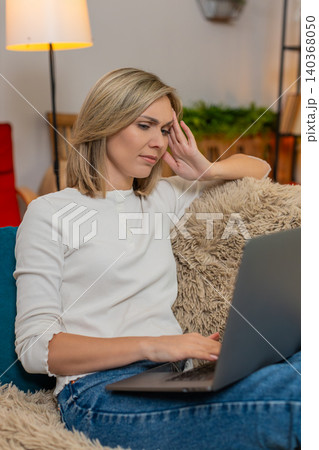 Woman massaging temples on sofa at home, feeling tired from long work on laptop headache discomfort 140368050