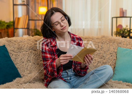 Girl writing heartfelt letter on paper at home, smiling with emotion before sealing it in envelope Girl writing heartfelt letter on paper at home, smiling with emotion before sealing it in envelope 140368068