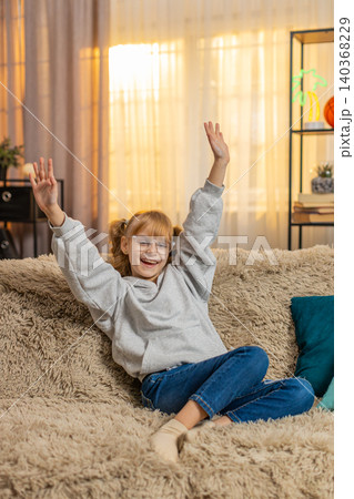 Young teenager girl celebrating victory with a joyful smile while looking at camera indoors at home 140368229