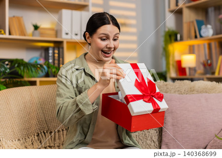 Young woman on home sofa opening gift box with joyful surprise and celebrating happy present at home Young woman on home sofa opening gift box with joyful surprise and celebrating happy present at home 140368699