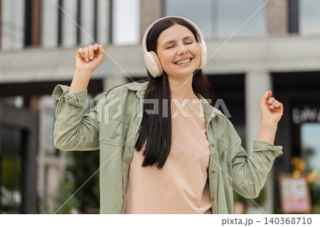 Young woman listening music walking in city street smiling and dancing with headphones in downtown 140368710