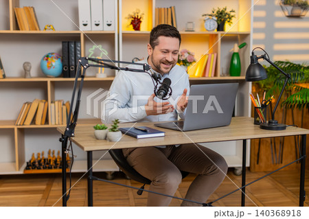 Young man on home table streaming live with laptop smiling and gesturing during online show at home 140368918