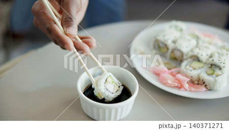 Hand, chopstick or sushi in home for dinner, Japanese cuisine or roll selection in living room. Hungry person, rice meal or soy sauce in dish to enhance flavor, seafood catering or platter in house 140371271