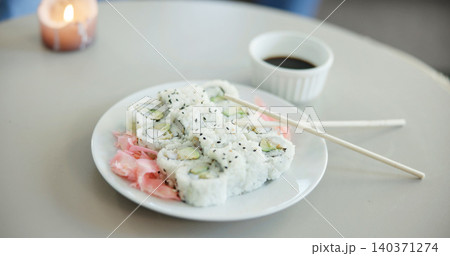 Food, chopsticks and sushi on plate for dinner, Japanese cuisine or soy sauce to enhance flavor. Meal, rice or pickled ginger on dish for appetizer, seafood catering and nutrition with candle in home 140371274