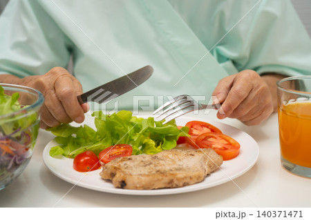 Asian elderly woman patient eating salmon stake and vegetable salad for healthy food in hospital. Asian elderly woman patient eating salmon stake and vegetable salad for healthy food in hospital. 140371471
