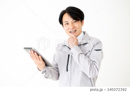 タブレットを見て驚くグレーの作業着のミドル男性ビジネスマン白バック タブレットを見て驚くグレーの作業着のミドル男性ビジネスマン白バック 140372392