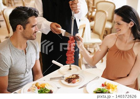 Couple, restaurant and waiter serving food or sausage kebab on skewer for fine dining, anniversary or nutrition. Man, woman and relationship bonding dates in Italy with water carving, meal or eating 140372626