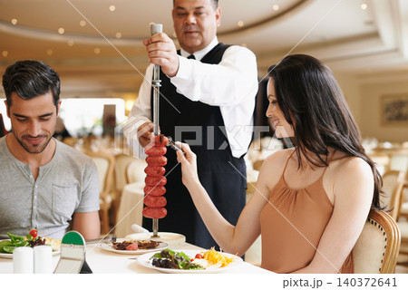 Couple, fine dining and waiter serving food or sausage kebab on skewer or restaurant, anniversary or nutrition. Man, woman and relationship bonding dates in Italy with water carving, meal or eating Couple, fine dining and waiter serving food or sausage kebab on skewer or restaurant, anniversary or nutrition. Man, woman and relationship bonding dates in Italy with water carving, meal or eating 140372641