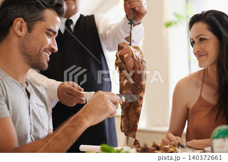 Couple, server and serving for dinner in restaurant with meat, happiness and fine dining for anniversary or honeymoon. Man, woman and employee with steak on skewer, healthy meal and table in London 140372661