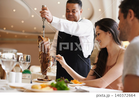 Couple, waiter and serving for dinner in restaurant with meat, happiness and fine dining for anniversary or honeymoon. Man, woman and employee with steak on skewer, healthy meal and table in London Couple, waiter and serving for dinner in restaurant with meat, happiness and fine dining for anniversary or honeymoon. Man, woman and employee with steak on skewer, healthy meal and table in London 140372664