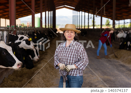 Elderly woman cow breeder standing in outdoor cowshed Elderly woman cow breeder standing in outdoor cowshed 140374137