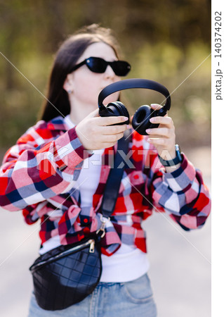 Young stylish woman adjusting headphones while listening to music outdoors Young stylish woman adjusting headphones while listening to music outdoors 140374202