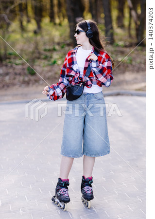 Young stylish girl enjoying music while roller skating in park Young stylish girl enjoying music while roller skating in park 140374203