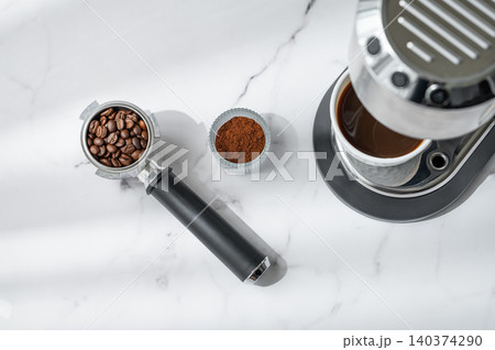 A flat lay of a cup of black coffee, a portafilter with roasted beans, ground coffee A flat lay of a cup of black coffee, a portafilter with roasted beans, ground coffee 140374290