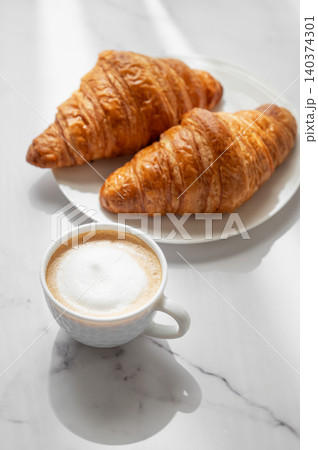 Freshly brewed cappuccino coffee in a cup on a white marble background with croissants 140374301