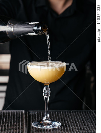 Bartender pouring sparkling cocktail into coupe glass close up 140374338