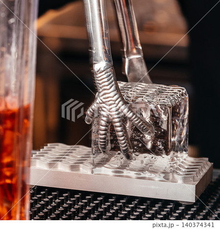 Metal ice tongs on crystal ice cube at cocktail bar close up Metal ice tongs on crystal ice cube at cocktail bar close up 140374341