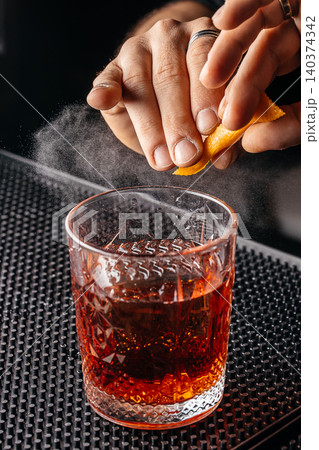 Bartender expressing orange peel over negroni cocktail in crystal glass Bartender expressing orange peel over negroni cocktail in crystal glass 140374342