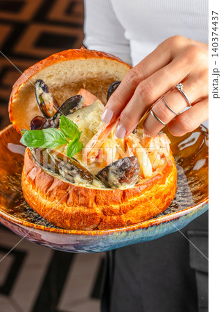 Hand taking shrimp from creamy seafood chowder served in artisan bread bowl Hand taking shrimp from creamy seafood chowder served in artisan bread bowl 140374437