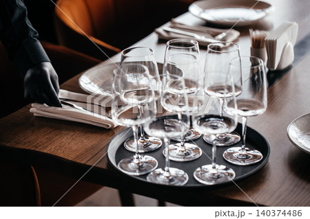 Waiter setting restaurant table with wine glasses and tableware for service 140374486
