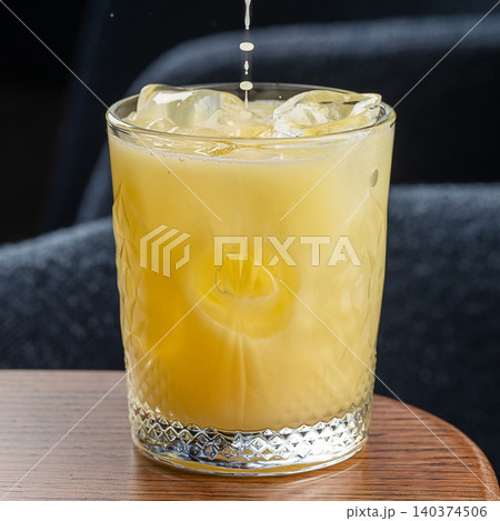 Fresh yellow citrus cocktail with ice cubes and falling splash in glass close up on dark background Fresh yellow citrus cocktail with ice cubes and falling splash in glass close up on dark background 140374506