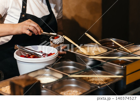 Preparing traditional Czech chimney cake dessert with strawberries and chocolate topping at street food stall Preparing traditional Czech chimney cake dessert with strawberries and chocolate topping at street food stall 140374527