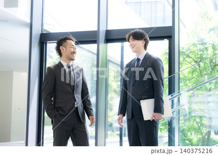 新緑のオフィスの窓際で会話する若手ビジネスマンと上司、取引先のコミュニケーションイメージ 140375216