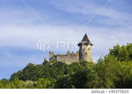 Salgo Castle ruins standing on forested hill under blue sky 140375623