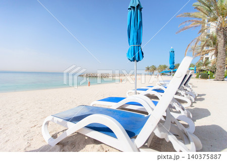 Beachside loungers arranged on a sunny day near calm waters and palm trees in a coastal paradise 140375887