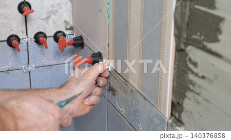 Worker Laying Ceramic Tiles on the Wall. Repairman Placing White Gray Square Tiles, Applying Adhesive. Builder Installing Tile Using Leveler, Tile Leveling Clips. Tiling. Finishing Repair Work. 4K 140376858