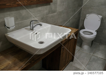 Modern faucet and water flow. Stylish white sink in a light interior. Chrome steel tap. Domestic Appliances. Gray clean bright bathroom. Household equipment. Grey vanity with tiled wall. Home interior Modern faucet and water flow. Stylish white sink in a light interior. Chrome steel tap. Domestic Appliances. Gray clean bright bathroom. Household equipment. Grey vanity with tiled wall. Home interior 140377105