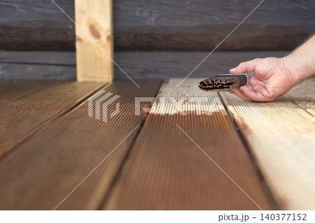 Brown oil for protection of wood by staining. Painting a larch for protecting and pests. Woodworker applying finish to terrace deck board. Repairman varnishing with brush wooden plank floor surface. 140377152