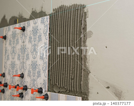 Worker Laying Ceramic Tiles on the Wall. Repairman Placing White Gray Square Tiles, Applying Adhesive. Builder Installing Tile Using Leveler, Tile Leveling Clips. Tiling. Finishing Repair Work. 4K 140377177