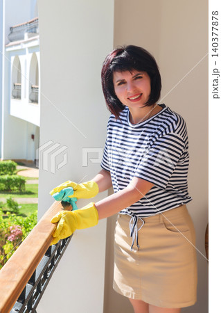 Beautiful brunette woman in casual clothes cleaning a sunny balcony terrace with urban view Beautiful brunette woman in casual clothes cleaning a sunny balcony terrace with urban view 140377878