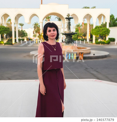 Woman standing in front of an elegant fountain with a grand arched entrance in the background Woman standing in front of an elegant fountain with a grand arched entrance in the background 140377879