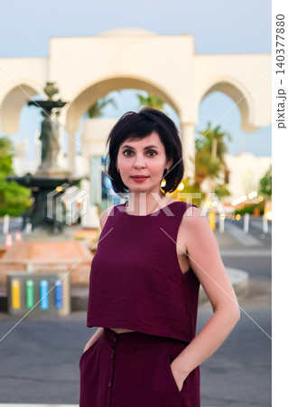 Woman standing in front of an elegant fountain with a grand arched entrance in the background Woman standing in front of an elegant fountain with a grand arched entrance in the background 140377880